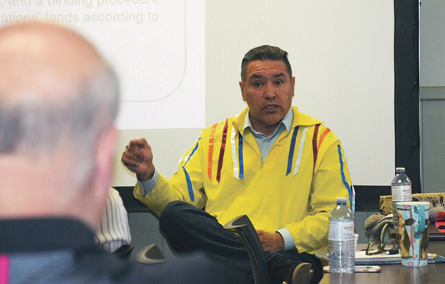 A person with a yellow traditional shirt, sitting and giving a presentation